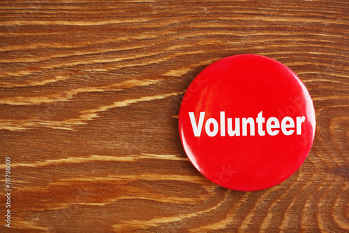 Round volunteer button on wooden background