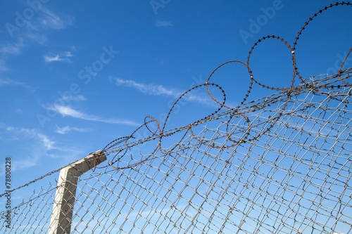 Metal fence with barbed wire over blue sky