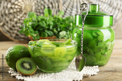 Tasty kiwi jam in glass bowl and jar on wooden background