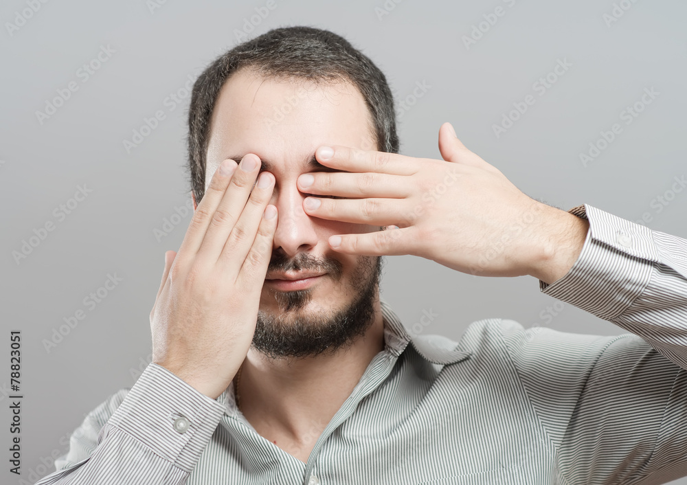 Fototapeta premium Portrait of a young man covering his eyes with hands