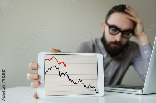 Depressed businessman leaning head below bad stock market chart photo