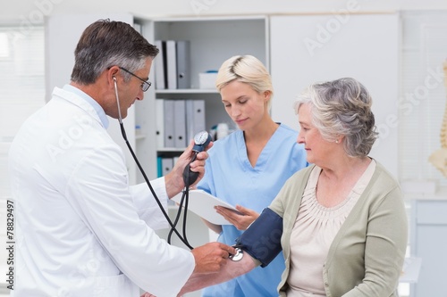 Doctor checking patients blood pressure while nurse noting it