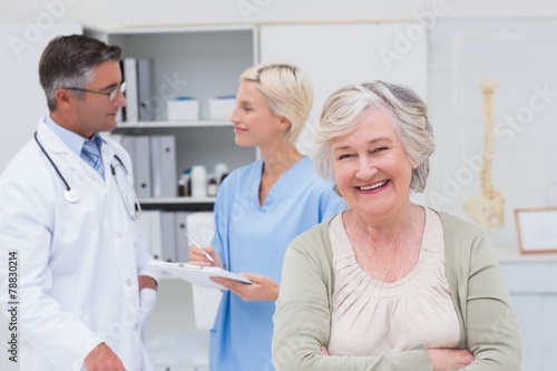 Patient smiling while doctor and nurse discussing in background © WavebreakmediaMicro