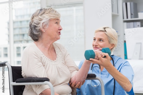 Nurse looking at patient while assisting her in lifting dumbbell