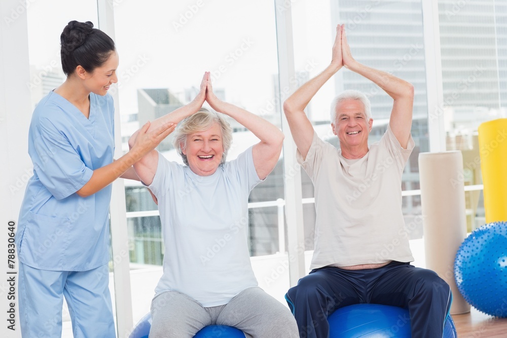 Obraz premium Senior couple on exercis ball being assisted by trainer