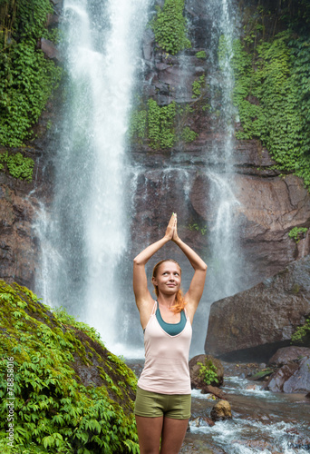 Young woman practicing yoga by the waterfall