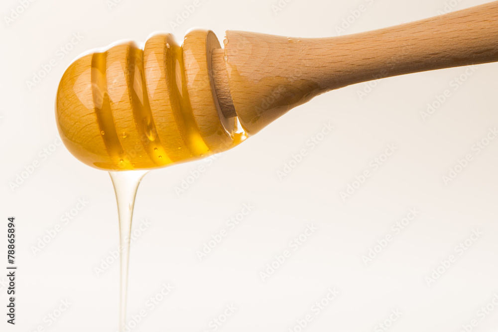 Honey dripping from a wooden honey dipper isolated on white back Honey dripping from a wooden honey dipper isolated on white back