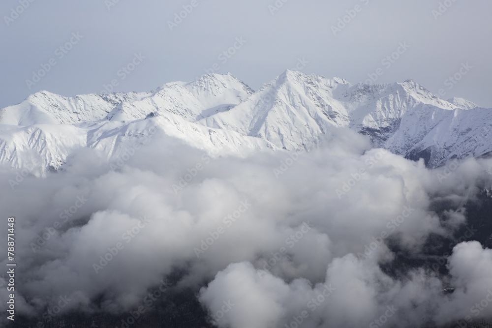 Tops of snow-capped mountains in the clouds.