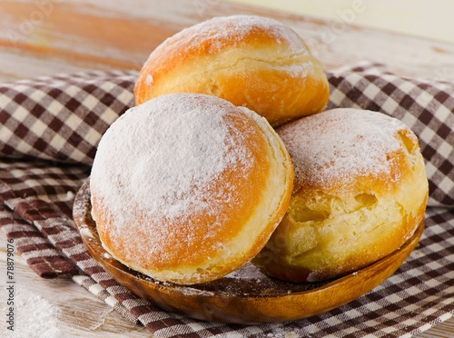 Sweet homemade Donuts with powdered sugar on a wooden plate.