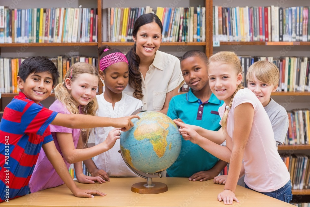 Fototapeta premium Cute pupils and teacher looking at globe in library