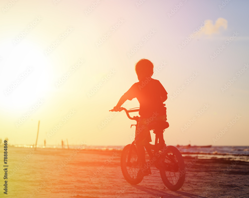 Naklejka premium little boy riding bike at sunset
