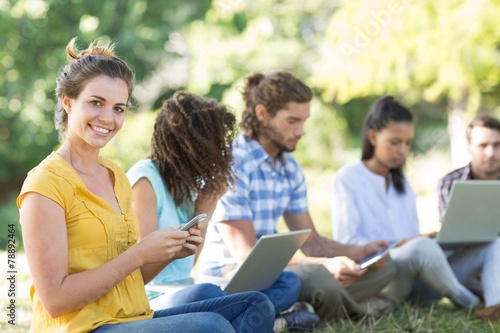 Smiling friends using media devices in park