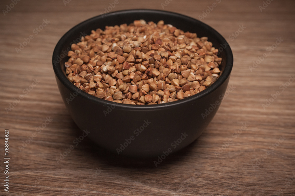 Buckwheat in black bowl on wooden background. Buckwheat in black bowl on wooden background.