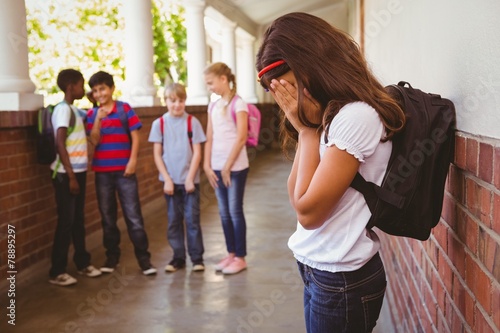 Sad schoolgirl with friends in background at school corridor