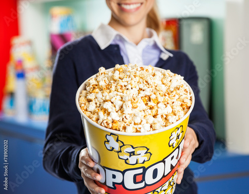 Worker Offering Popcorn Bucket At Cinema Concession Stand