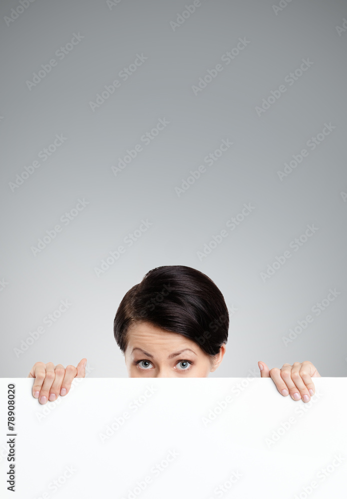 Beautiful woman hides behind a huge sheet of white cardboard Beautiful woman hides behind a huge sheet of white cardboard