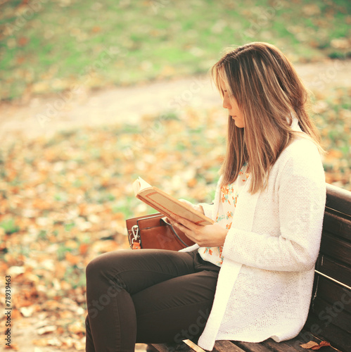 Woman reading a book at bench in autumn park