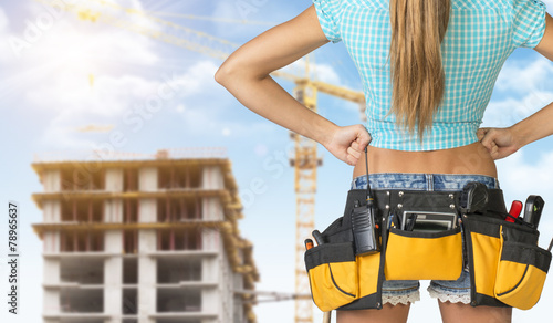 Woman in tool belt standing backwards, akimbo. Cropped image