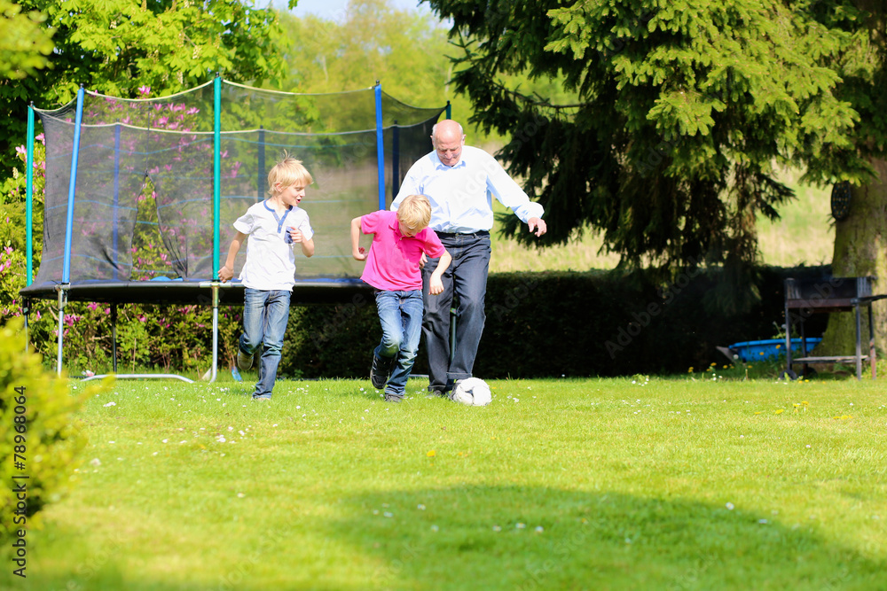 Active grandfather playing soccer with grandsons in the garden