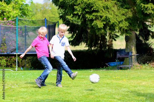 Two happy brothers playing soccer in the garden