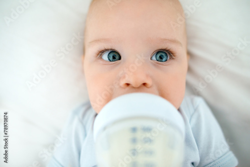 beautiful baby lying on his back in bed drinking milk