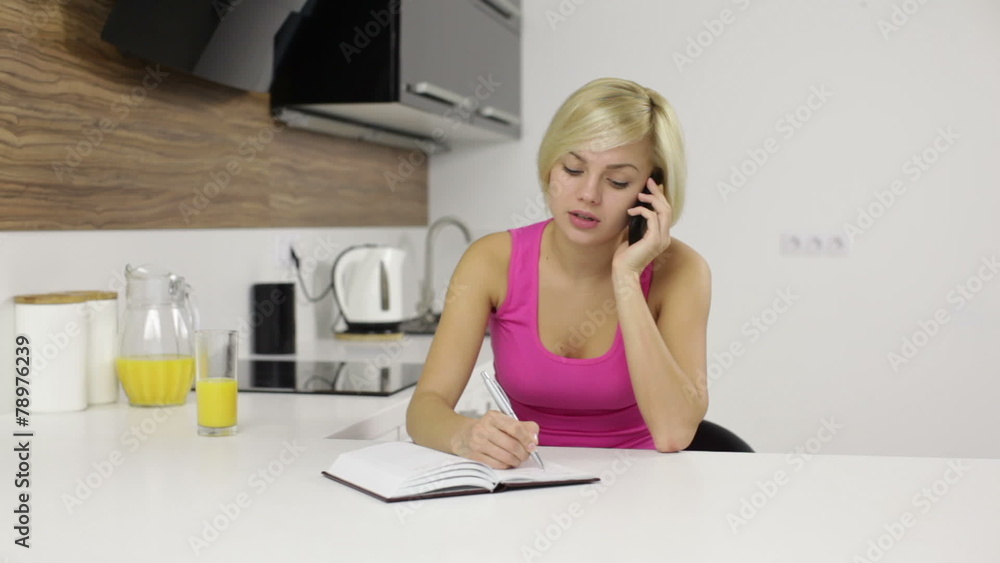 Woman speaking mobile phone call kitchen, make note writing Woman speaking mobile phone call kitchen, make note writing