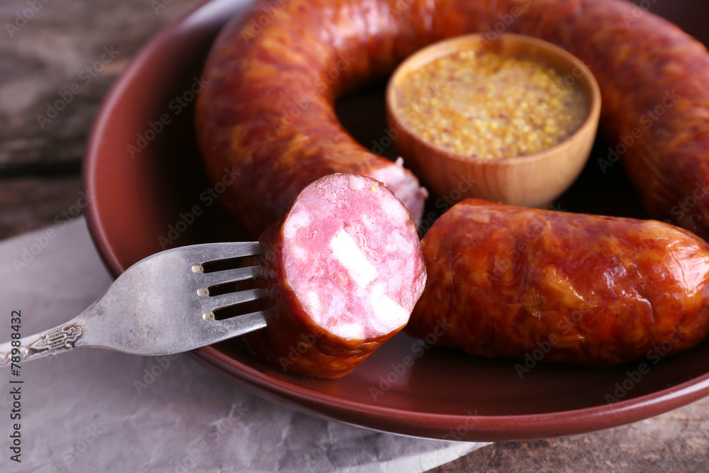 Smoked sausage with mustard on plate on wooden table, closeup