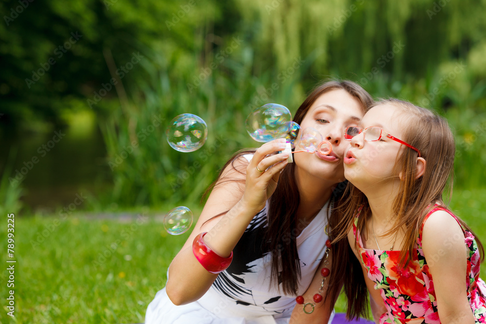 Mother and little girl blowing soap bubbles in park. Mother and little girl blowing soap bubbles in park.