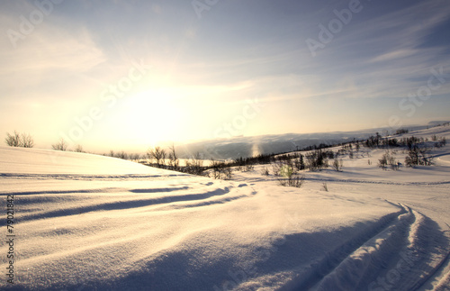 Snow covered Norwegian mountain tracks with warm sun set glow.