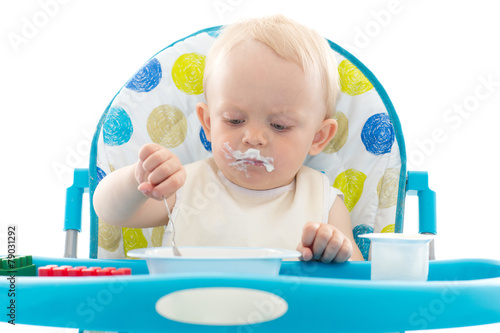 Sweet baby with spoon eats the yogurt.