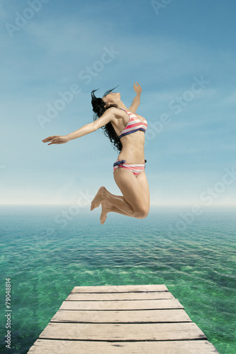 Excited woman in swimsuit jumps at pier