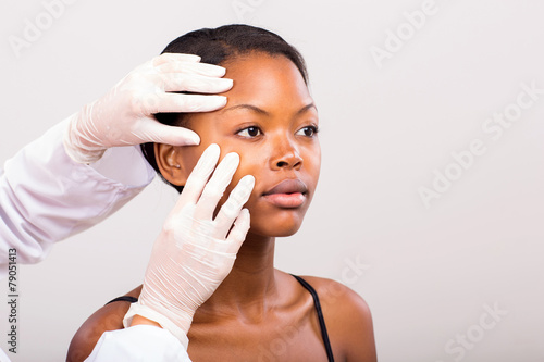 dermatologist checking young african american woman face skin photo