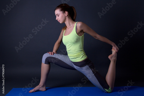 young beautiful sporty woman stretching legs over grey