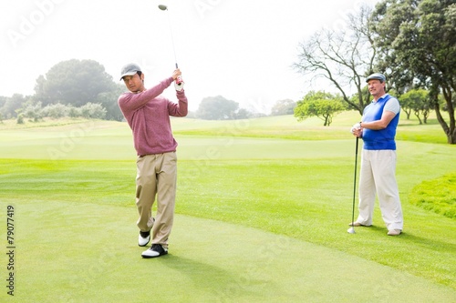 Golfer swinging his club with friend behind him