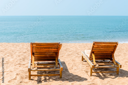 couple of empty chairs on a sandy beach in the afternoon