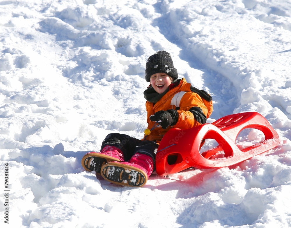 Child plays with red sled in the snow in winter