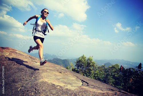 woman hiker running at on mountain peak rock