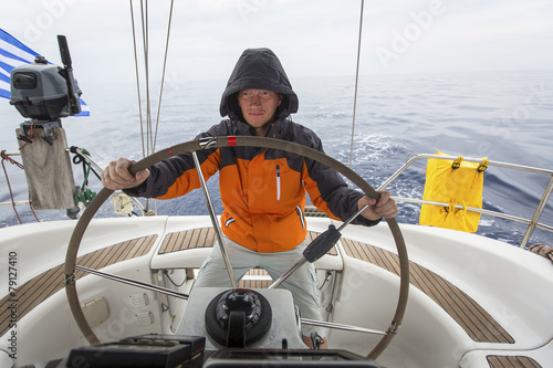 Young man skipper in the sea at the helm of a sailing yacht.