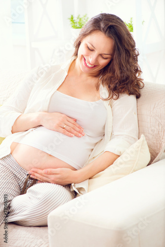Pregnant happy woman sitting on a sofa and caressing her belly