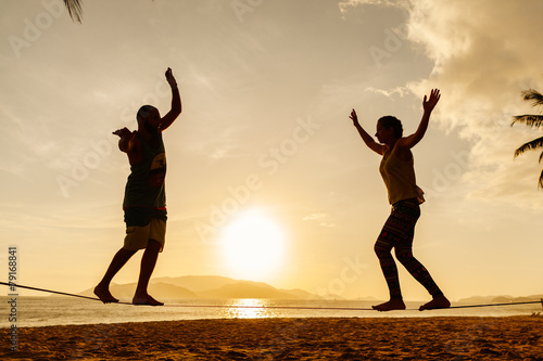 Bild auf Leinwand teenage couple balancing slackline on the beach