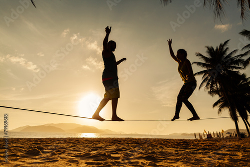 teenage couple balancing slackline on the beach photo