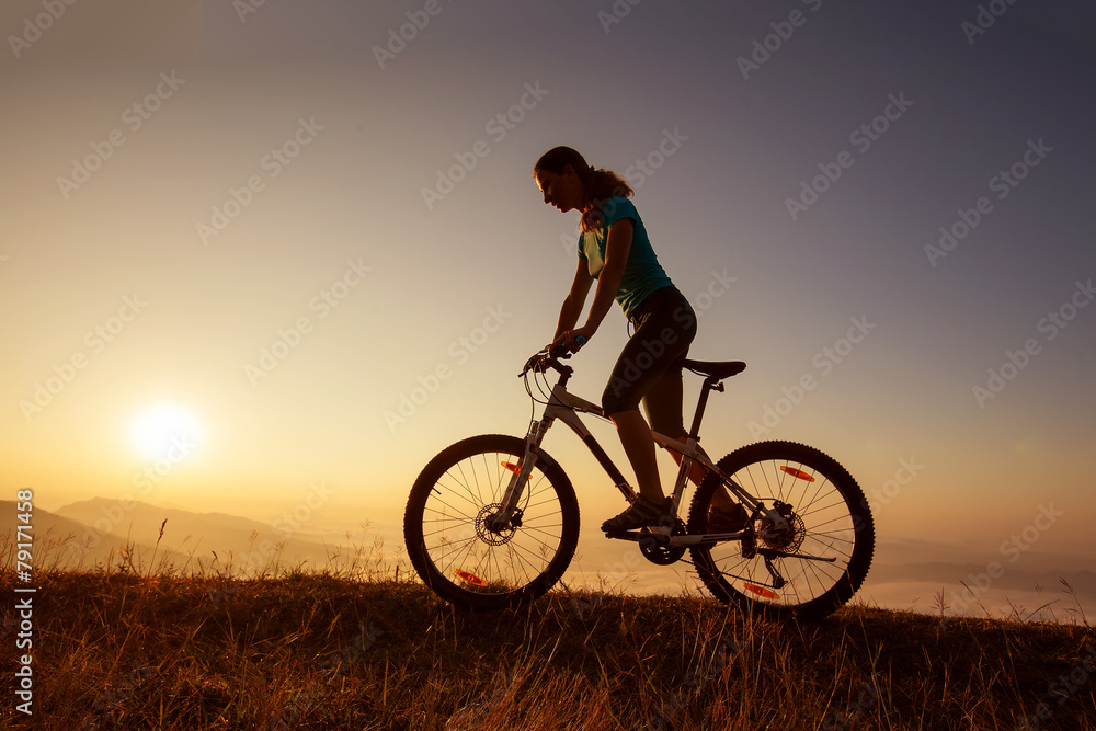 Fototapeta premium Biker-girl at the sunset on mountains