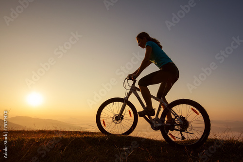 Fototapeta Naklejka Na Ścianę i Meble -  Biker-girl at the sunset on mountains