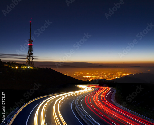 car lights at night towards the city and communications antenna