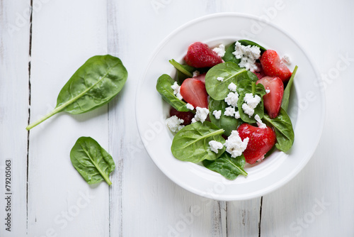 Salad with spinach, strawberry and cheese, white wooden surface