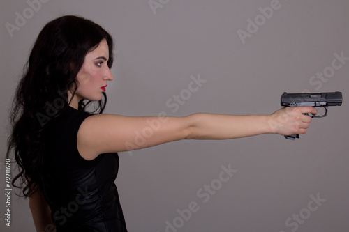 side view of young beautiful woman with gun over grey