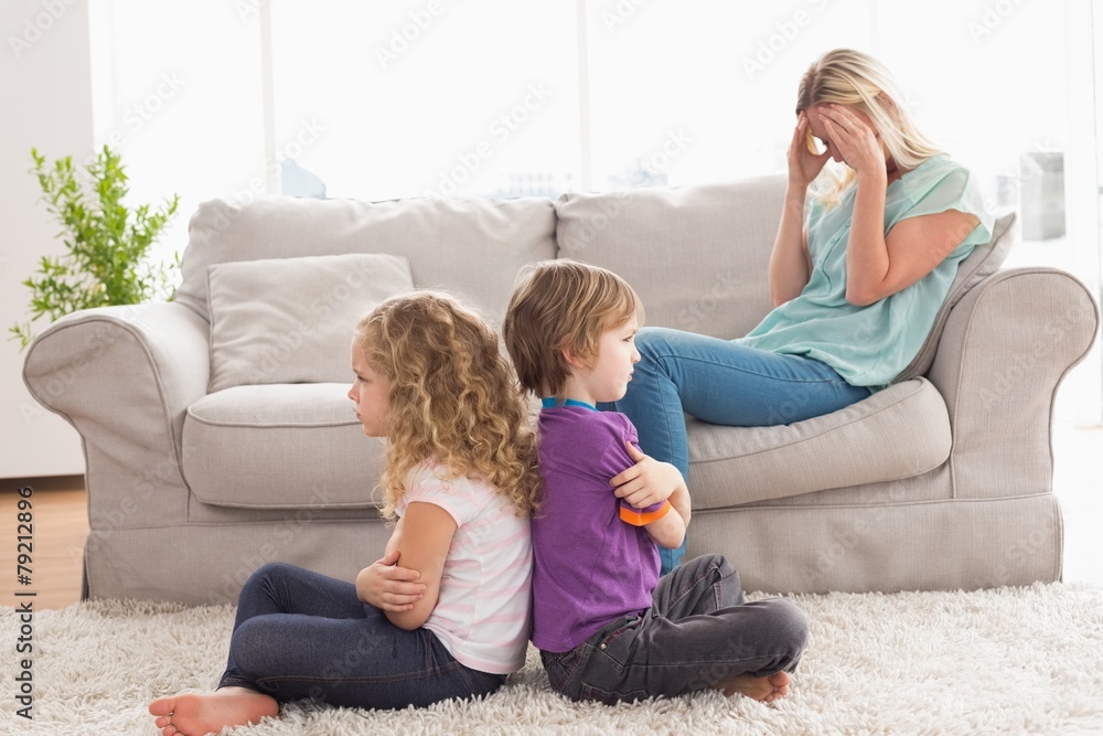 Angry siblings sitting arms crossed with upset mother on sofa