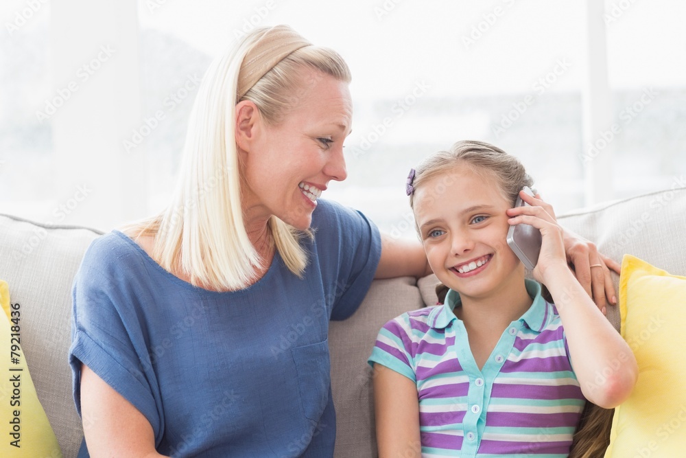 Mother looking at daughter using mobile phone on sofa Mother looking at daughter using mobile phone on sofa