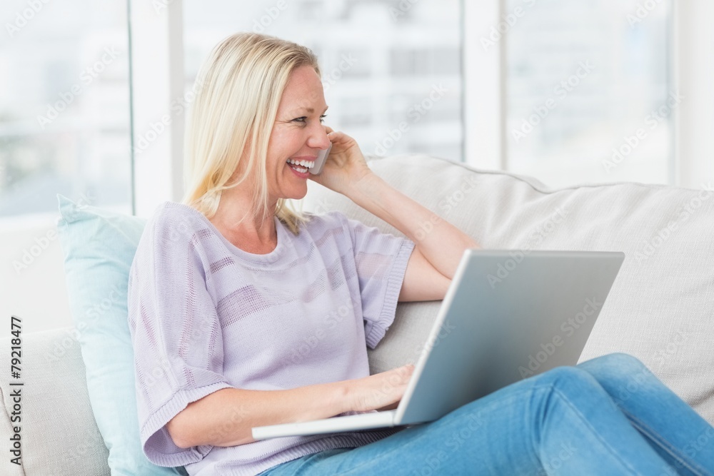 Woman talking on mobile phone while using laptop on sofa Woman talking on mobile phone while using laptop on sofa