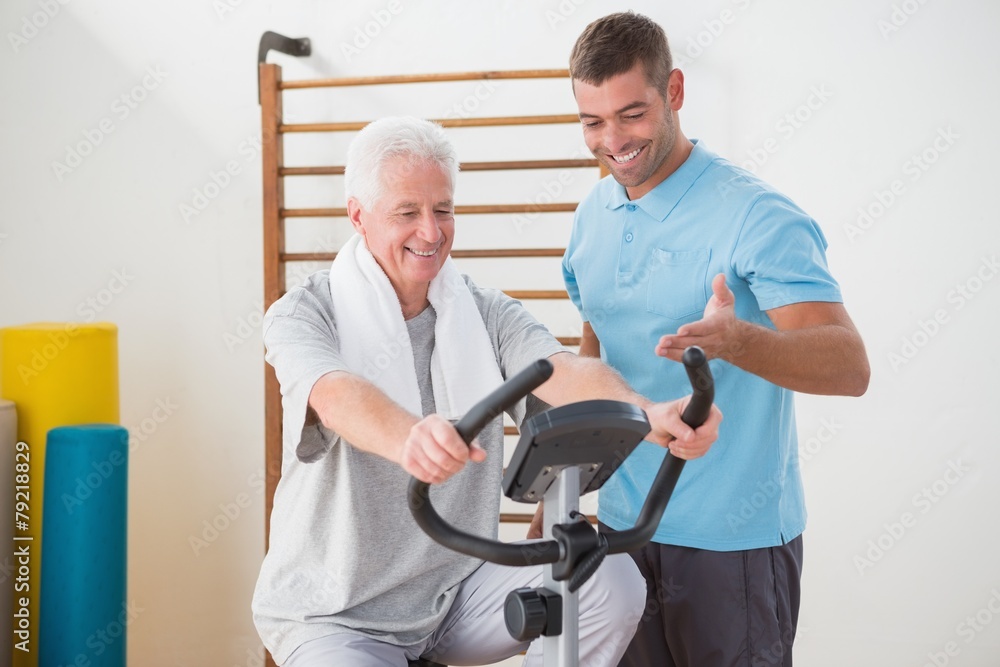 Senior man doing exercise bike with his trainer Senior man doing exercise bike with his trainer